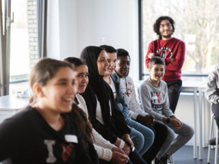 Leerlingen en vrijwilliger kijken aandachtig naar een gastles van Soufian Touzani die buiten beeld les geeft.